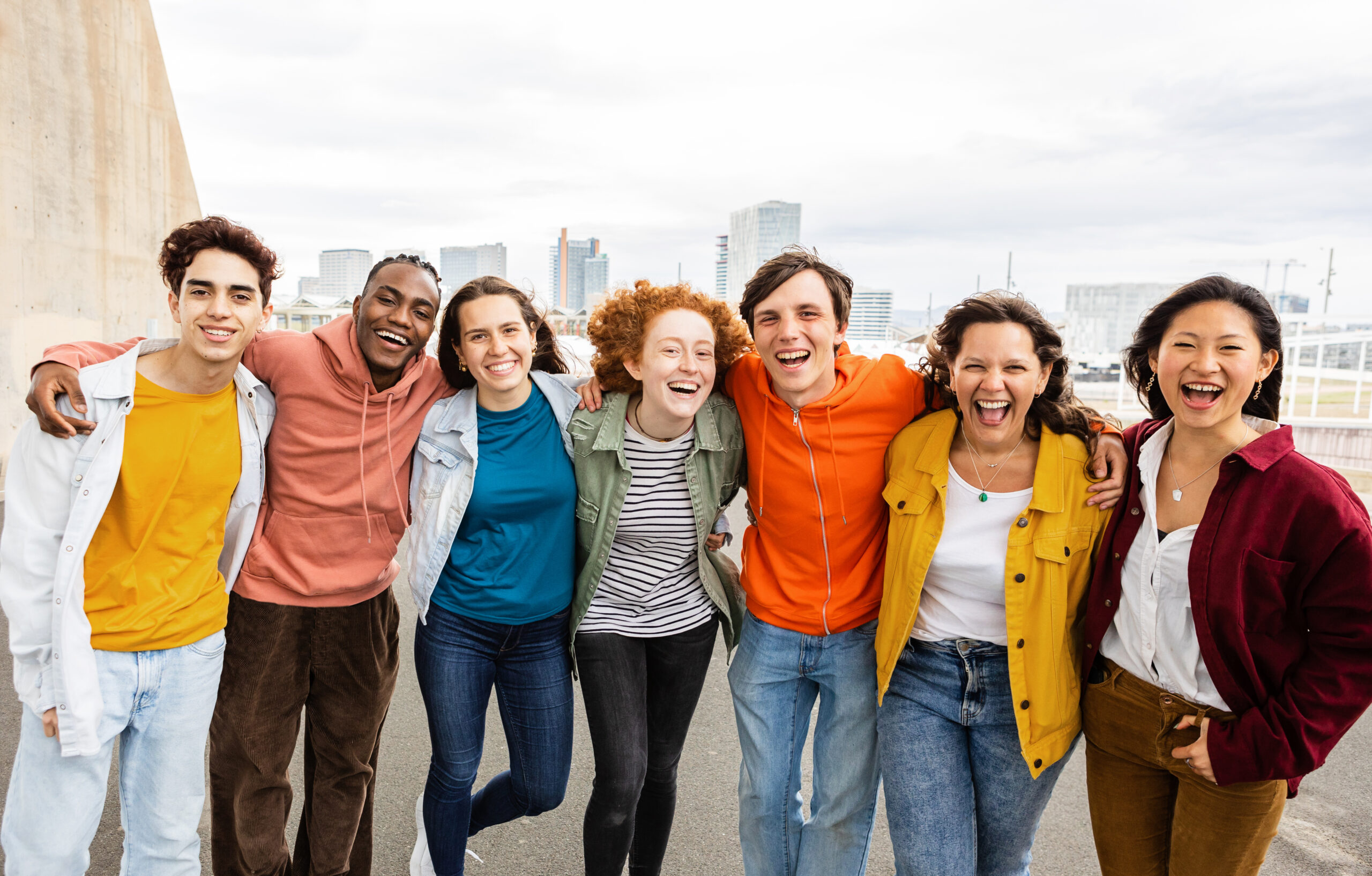 Happy group portrait of student teen friends hugging each other smiling at camera outside. Diverse teenagers having fun outdoors. Youth and millennial people concept