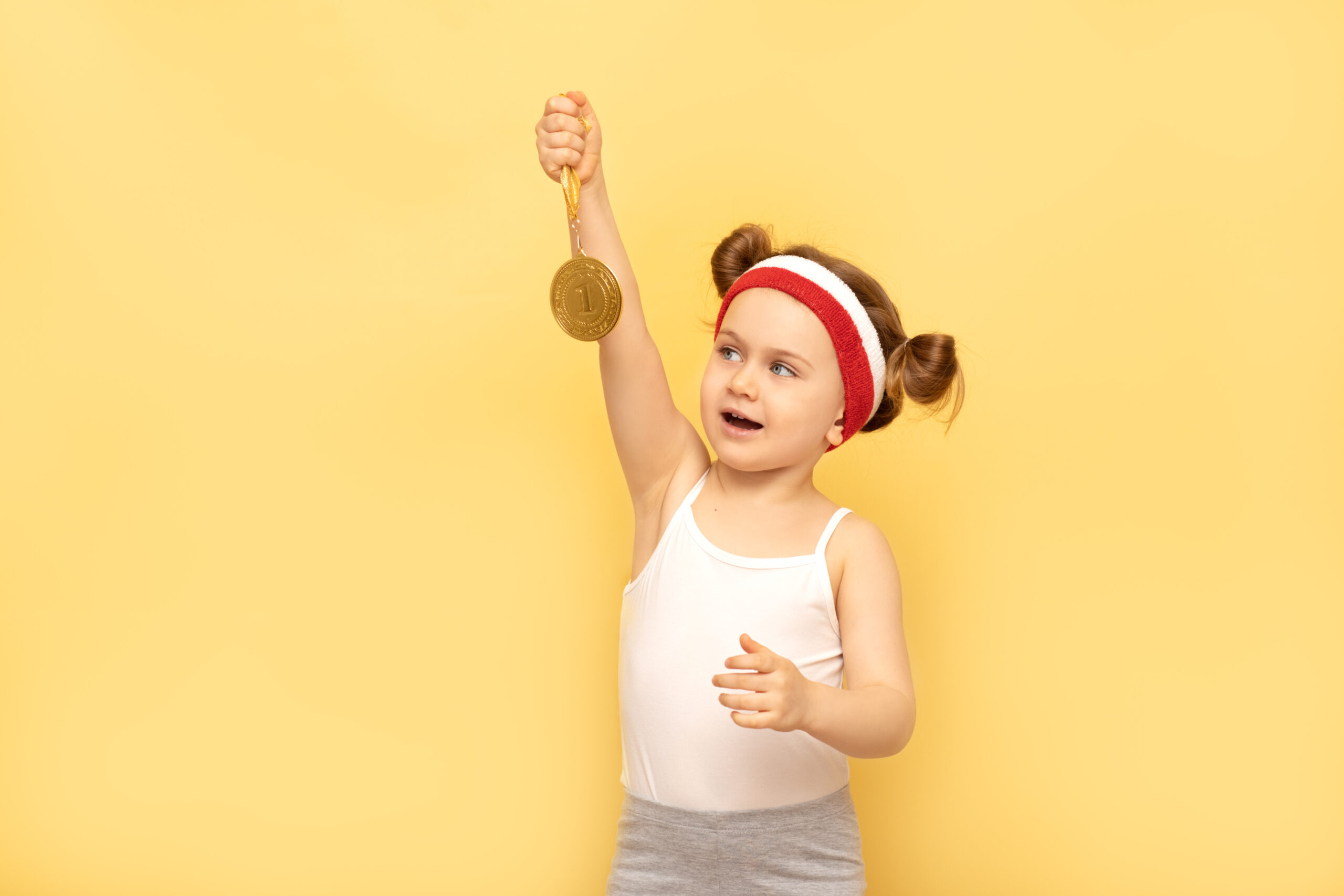Smiling toddler wearing workout gear while holding a medal