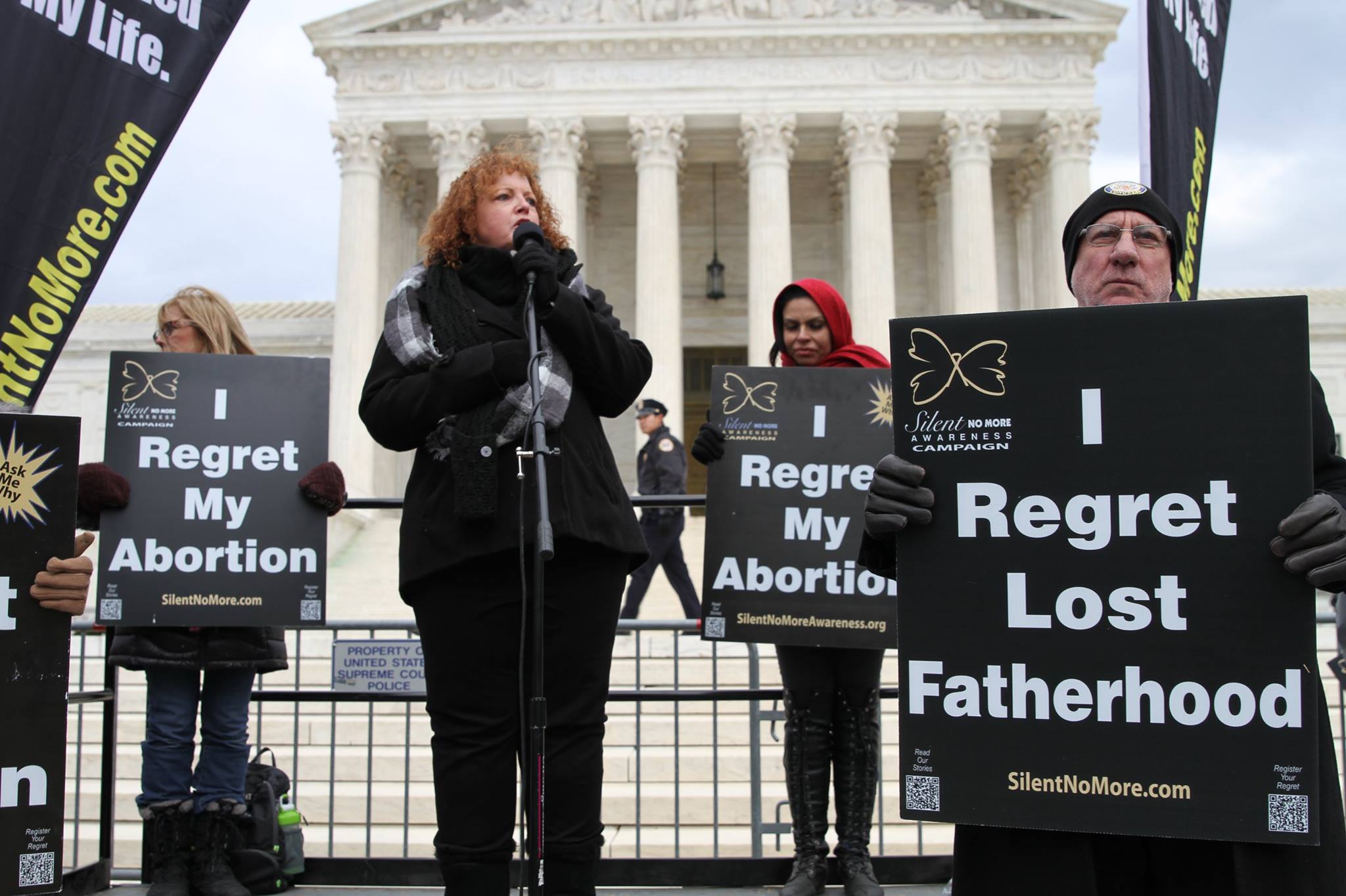 Woman speaking in front of the supreme court building and man holding "I regret lost fatherhood" sign.