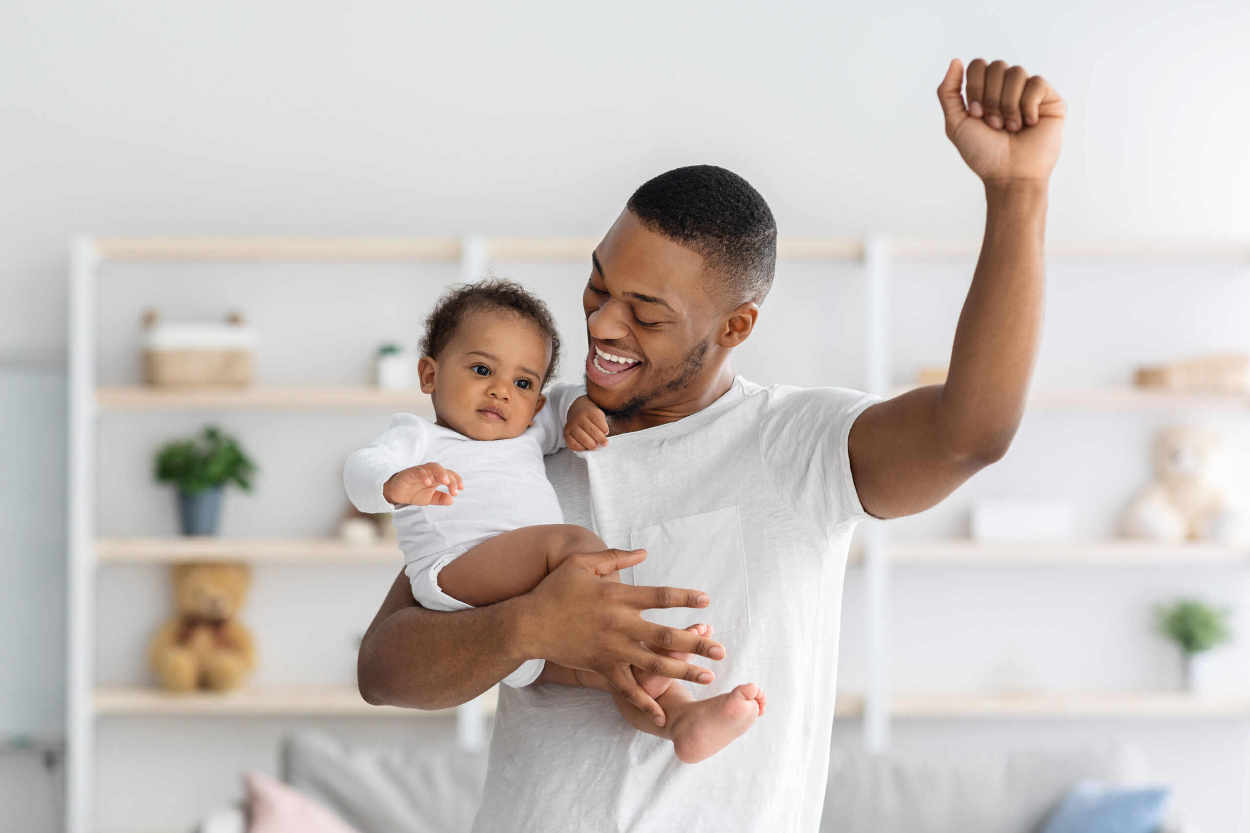 Happy African American Father Holding Adorable Toddler Baby, Raising Hand And Exclaiming With Excitement