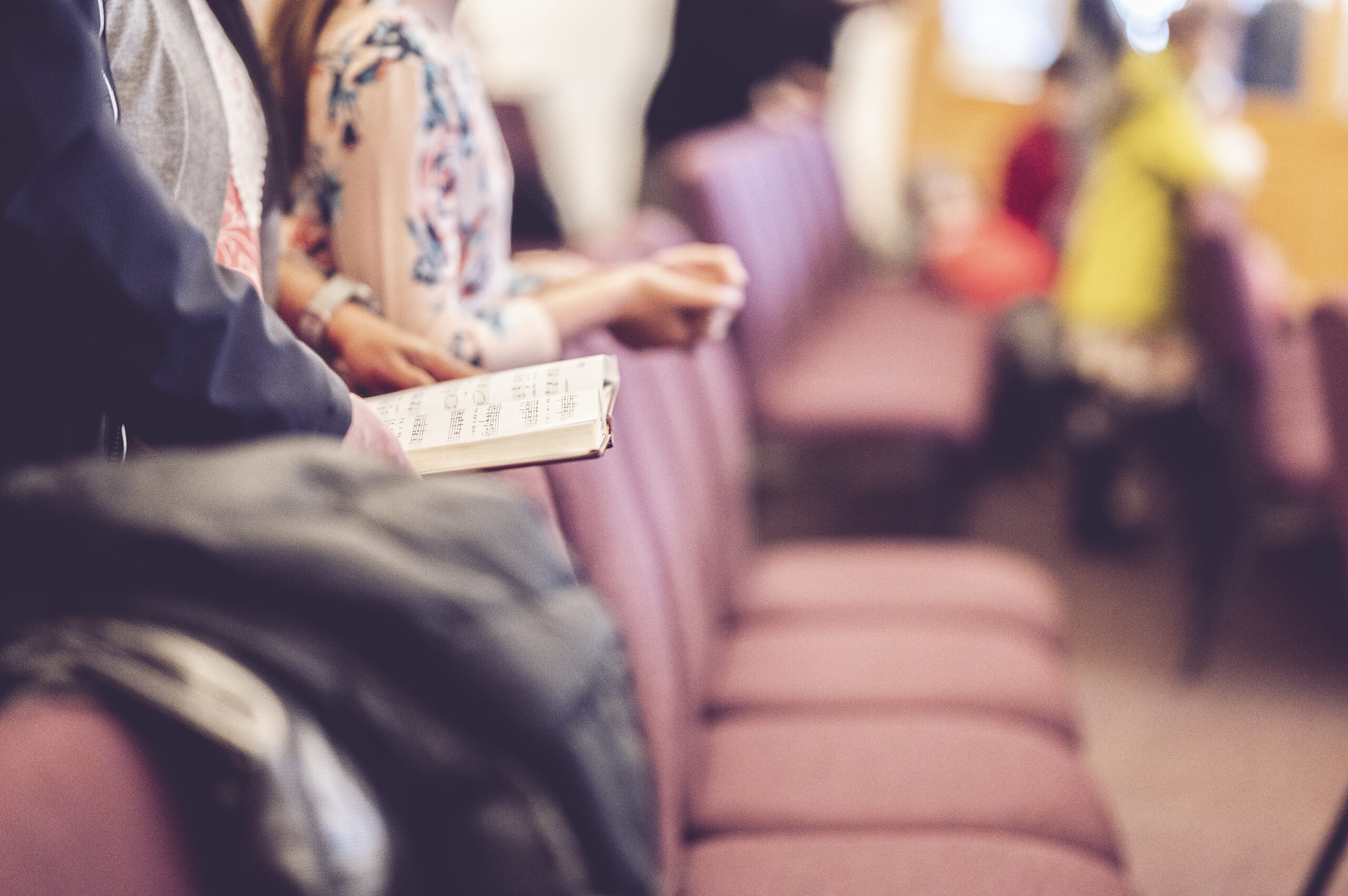 A selective focus shot of a man in long sleeves holding a songbook in the church