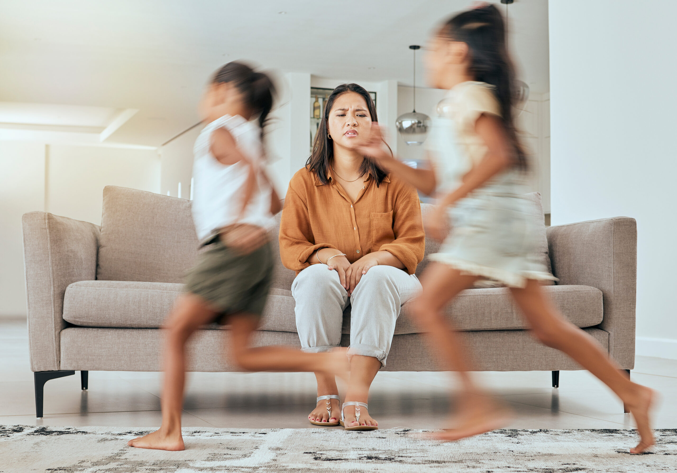 Mother stressed out while children run around the room.